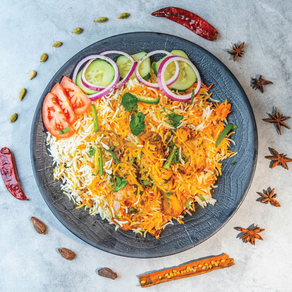 Chicken biryani plated with spices, cucumber and onion